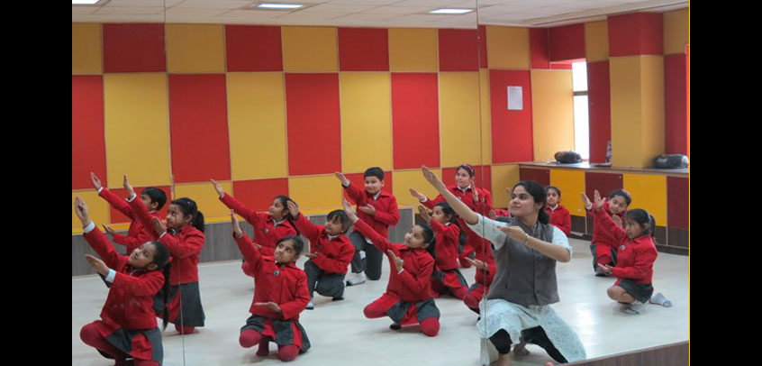 the image shows teacher teaching dance to girl students,school with theatre
