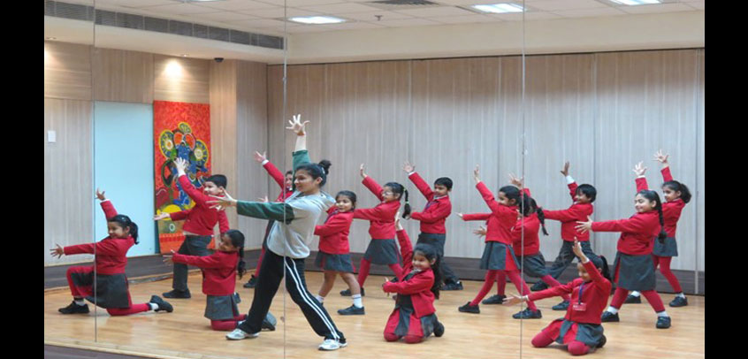 the image shows teacher teaching dance to girl students,school with theatre
